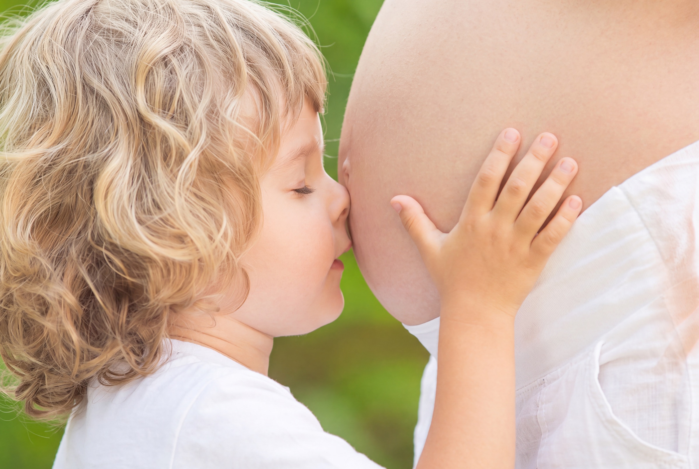 Kind küsst den Bauch der schwangeren Mutter